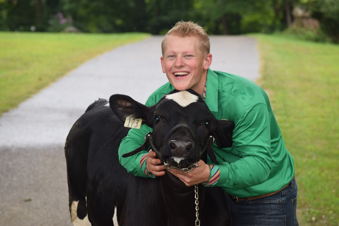 A young blond man in a green shirt hugging a black and white calf.